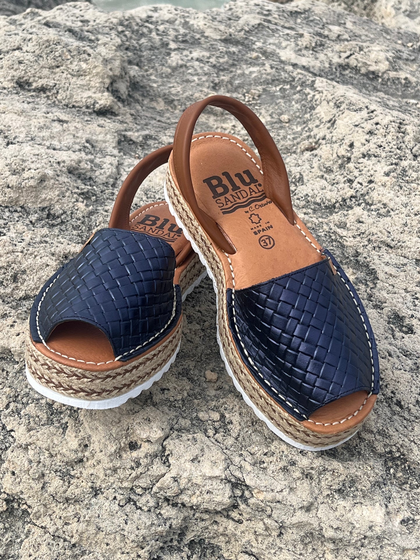 Pair of navy blue sandals with brown straps on a stone surface
